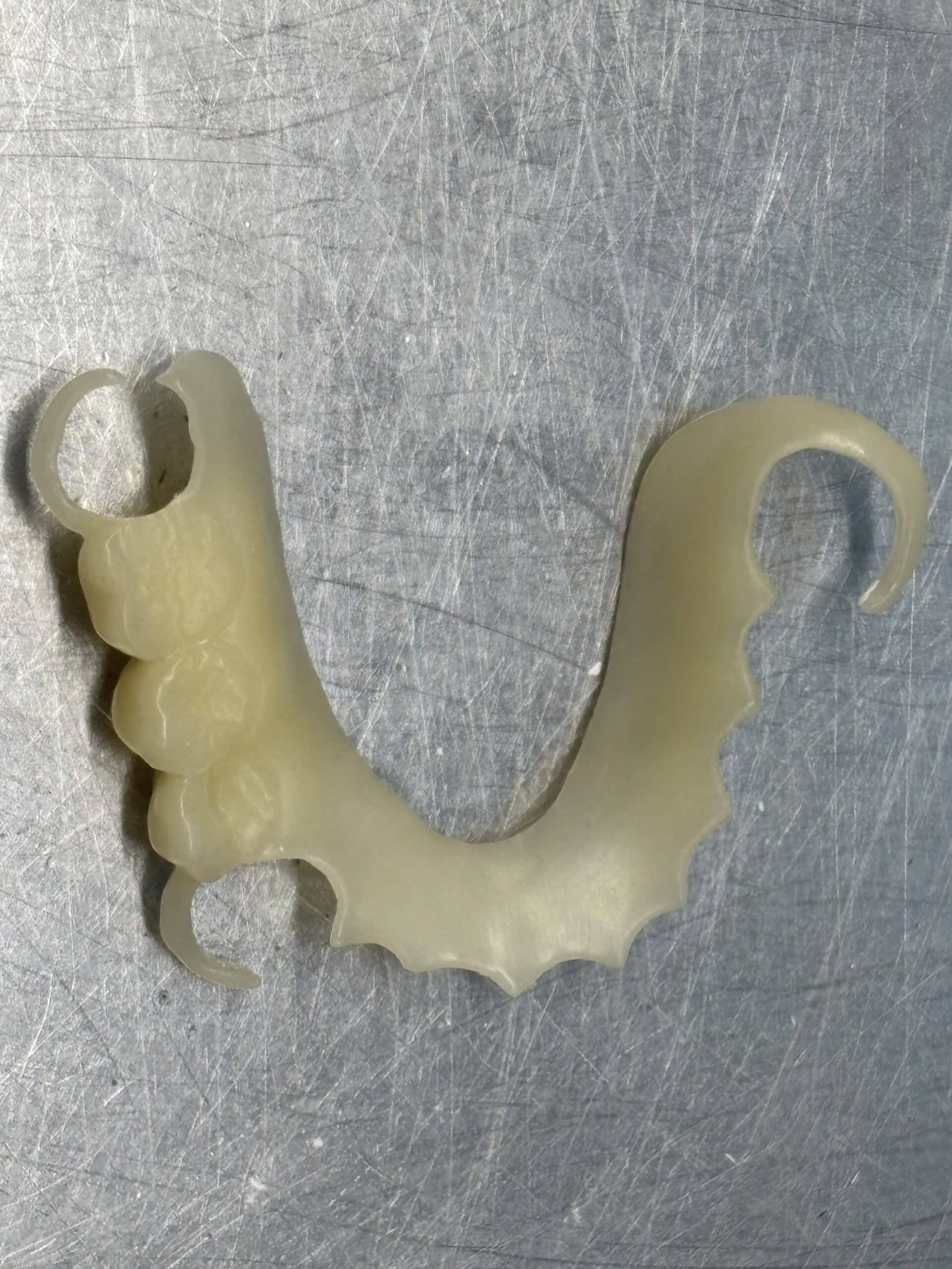 Prothèse dentaire partielle amovible translucide avec dents artificielles sur surface métallique rayée.